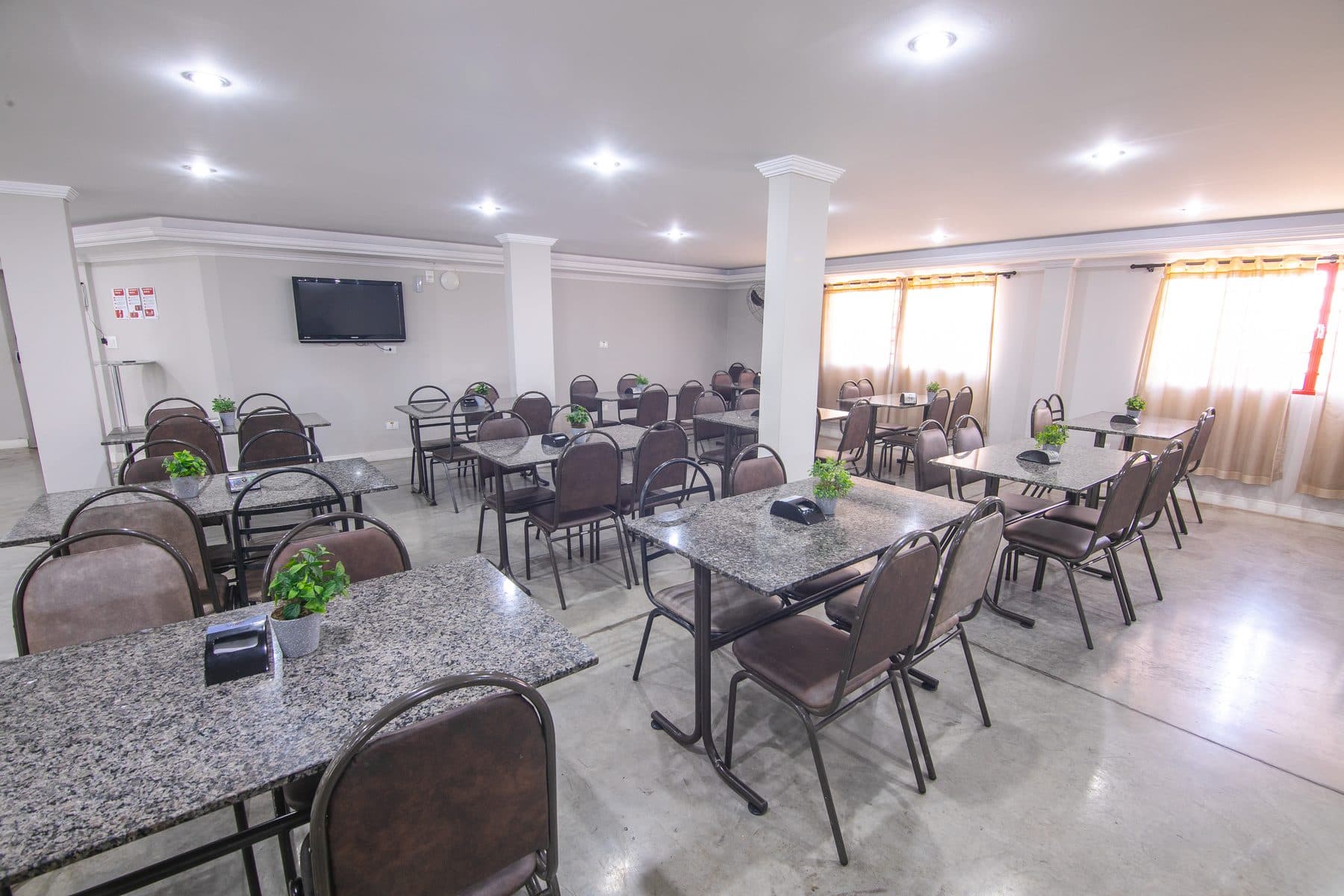 Salão de refeições do Hotel Galli, com mesas e televisão